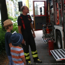Zwei Kinder lassen sich von einem Feuerwehrmann das Innere eines Hilfeleistungs- und Löschfahrzeugs zeigen.