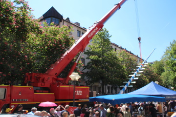 Der Kranwagen der Berufsfeuerwehr zieht den Maibaum nach oben.